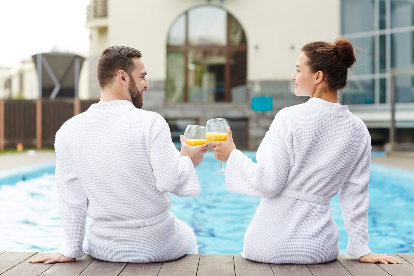 Idyllic couple toasting with glasses of juice while sitting by swimming-pool